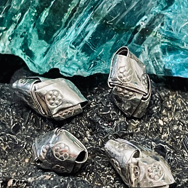 May include: Four silver metal beads with a textured surface and a floral design. The beads are arranged on a dark background.