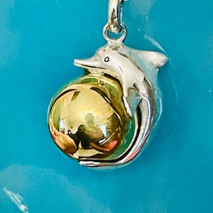 May include: A silver dolphin charm pendant with a gold orb inside. The dolphin is holding the orb with its fins and tail.