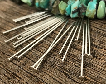 Puede incluir: Primer plano de un grupo de alfileres de cabeza plateada dispuestos en forma de abanico sobre una superficie de madera. Los alfileres son todos del mismo tamaño y tienen una cabeza redondeada.