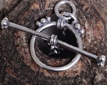 May include: A silver toggle clasp with a black circular center. The clasp features a bar with rounded ends and a ring for attachment. The design includes decorative beaded accents around the circular portion.