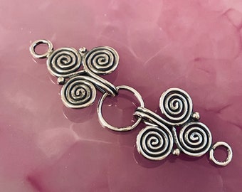 May include: Silver-toned metal clasp with a decorative spiral design. The clasp features two sets of three spirals connected by a ring, with a small loop on each end. The piece is set against a pink background.
