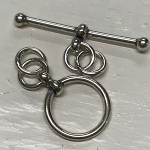 May include: Silver tone toggle clasp with a round ring and a bar with two round ends.