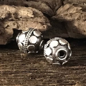 May include: Two silver beads with a textured, circular design. The beads have a raised, circular pattern.