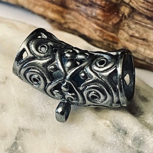 May include: A silver-toned metal bead cap with an intricate, ornate design. The bead cap has a loop on the bottom for attaching to a cord or chain.