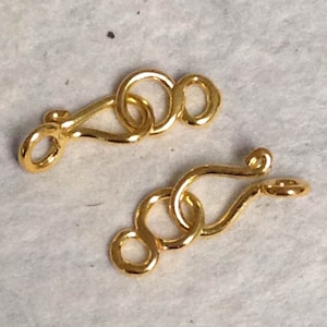 May include: Two gold-toned metal clasps with a looped design. Each clasp has a hook and a loop for attaching to a necklace or bracelet.