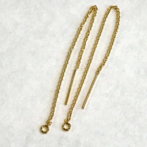 May include: A pair of gold-colored chain earrings. Each earring features a delicate chain with a straight bar and a small circular loop at the end. The earrings are displayed against a white background.