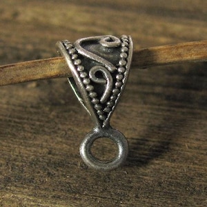 Könnte beinhalten: Silberfarbener Metall-Anhänger-Bügel mit einem dekorativen Wirbelmuster und einem Perlenrand. Der Bügel hat unten eine Schlaufe zum Anbringen eines Anhängers.