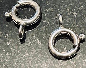 May include: Two silver-toned metal lobster clasps, each with a circular ring and a spring-loaded latch. These clasps are commonly used for jewelry making and other craft projects.