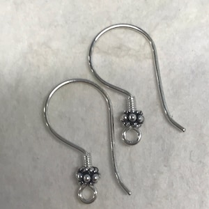 May include: A pair of silver-colored earring hooks. Each hook has a curved wire design with a decorative cluster of small, round beads near the bottom. The earrings are designed for pierced ears and are displayed against a neutral background.