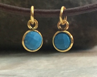 May include: Two gold charms with blue turquoise stones. The charms are round and have a simple design.