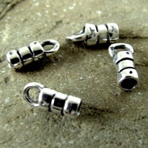 May include: Four silver-toned metal end caps for jewellery making. Each cap has a cylindrical shape with a decorative pattern and a small loop at the top.