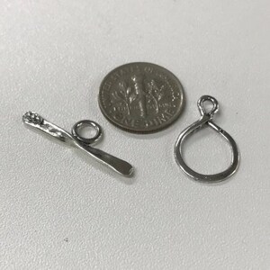 May include: Two silver metal jewelry findings, one is a twisted bar with a loop at one end, the other is a simple loop. A US dime is included for size comparison.