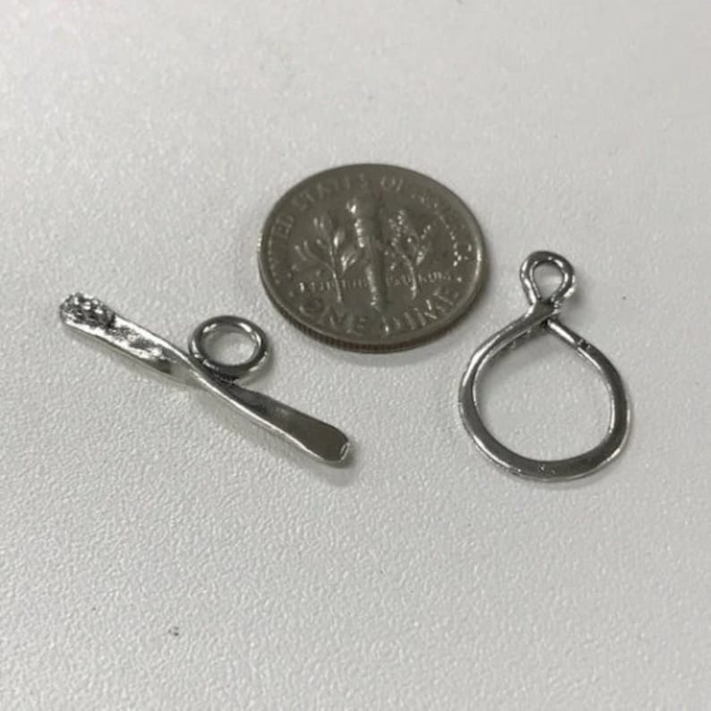 May include: Two silver metal jewelry findings, one is a twisted bar with a loop at one end, the other is a simple loop. A US dime is included for size comparison.