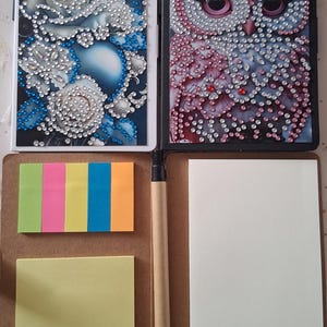 Peut inclure: Carnet ouvert avec deux couvertures décoratives. L'une présente des roses blanches avec des accents bleus en strass, l'autre un hibou avec des strass roses et argentés. Comprend des post-it, un stylo et des pages vierges.