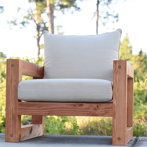 Puede incluir: Una silla de madera con un acabado marr&oacute;n claro y un coj&iacute;n blanco. La silla tiene un dise&ntilde;o simple y moderno y es perfecta para uso en exteriores.