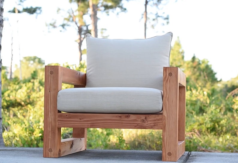 Puede incluir: Una silla de madera con un acabado marr&oacute;n claro y un coj&iacute;n blanco. La silla tiene un dise&ntilde;o simple y moderno y es perfecta para uso en exteriores.