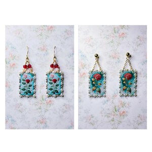 May include: Two pairs of earrings with a floral design. The earrings are made of gold and have a blue background with red roses. The earrings are surrounded by white pearls.