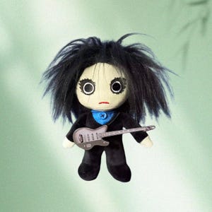 May include: A handmade doll with a pale face, large black eyes, and black messy hair. The doll wears a black outfit with a blue collar and holds a silver guitar. The doll is a unique, handcrafted item.