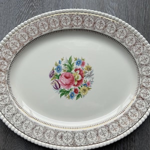 Puede incluir: Fuente ovalada para servir con base blanca, con un ramo floral en el centro con rosas rosas y otras flores coloridas. El borde tiene un diseño dorado y marrón adornado con un borde de cuentas.