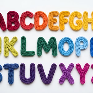 May include: A collection of colorful, crocheted letters of the alphabet, arranged in three rows. The letters are in various colors, including red, orange, yellow, green, blue, purple, and pink. The letters are handmade and have a textured appearance.