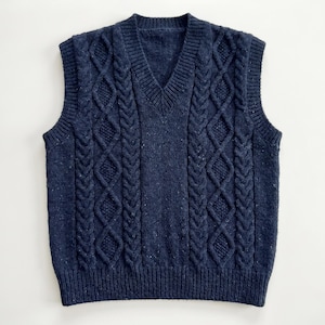 May include: A navy blue cable-knit sweater vest with a V-neck. The vest features a textured pattern with vertical cable designs and a ribbed hem. The sleeveless garment is made of a soft, speckled yarn.