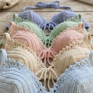 May include: A collection of handmade crochet bikini tops in pastel colors: light blue, green, pink, and cream. Each top features a scalloped edge and tie closure, perfect for beachwear or summer fashion.