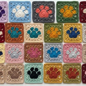 May include: A collection of twenty-five crocheted squares, each featuring a paw print design. The squares are in various colors, including purple, blue, gray, orange, yellow, and brown. The paw prints are in contrasting colors, creating a visually appealing pattern.