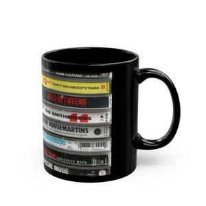 May include: Black ceramic coffee mug featuring a stack of vintage cassette tapes. The tapes include titles like "Junk Culture," "Party Mix/Mesopotamia," and "Greatest Hits." A classic music-themed gift.