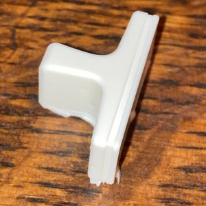 May include: White plastic door handle with a T-shaped design. The handle has a smooth, matte finish.