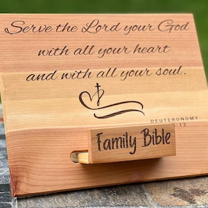May include: Wooden Bible stand with engraved text: "Serve the Lord your God with all your heart and with all your soul." Includes a small drawer labeled "Family Bible." The stand is made of light-colored wood.