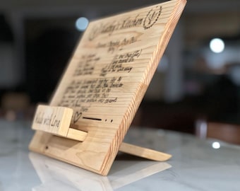 May include: A wooden recipe stand with a handwritten recipe on the front. The stand is made of light wood and has a small heart carved into the front. The text on the stand reads "Made with Love".