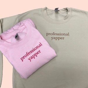 May include: Two sweatshirts, one pink and one beige, both with the text "professional yapper" printed on them.