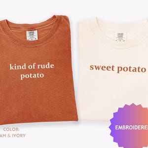 May include: Two t-shirts, one yam-colored and one ivory-colored, are displayed. The yam-colored shirt reads "kind of rude potato" in white text. The ivory shirt says "sweet potato" in brown text. A purple and pink embroidered tag is visible.