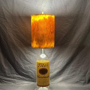 May include: A lamp made from a Tito's Handmade Vodka bottle with a brown and orange lampshade.