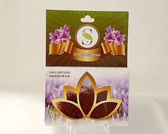 May include: A white box with a gold and green label that says "Finest Saffron" and a picture of saffron flowers. The box is labeled "100% NATURAL PACKED IN U.K." and has a clear window showing red saffron threads inside a gold lotus flower design.