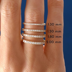 May include: A hand displays four gold rings, each set with small gemstones. The rings are of varying widths, labelled with sizes: 1.30 mm, 1.50 mm, 1.80 mm, and 2.00 mm. The background is a deep blue.