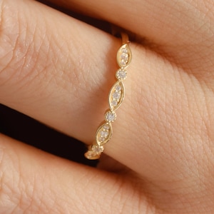 Peut inclure: Une fine bague en or présentant une série de montures alternées en forme de marquise et rondes, chacune contenant une petite pierre précieuse claire. L'anneau a une finition métallique polie et suit un motif géométrique répétitif.