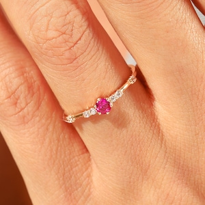 May include: A delicate gold ring with a single pink gemstone surrounded by smaller clear gemstones.