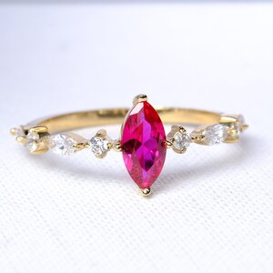 May include: A gold ring with a large, marquise-shaped, pink gemstone surrounded by smaller, clear gemstones.