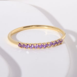 May include: A gold band ring with a row of small purple gemstones.