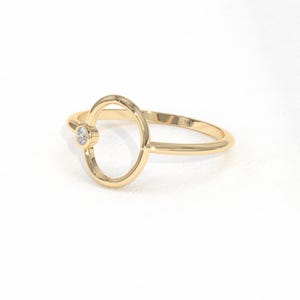 Puede incluir: Un anillo de oro con un dise&ntilde;o ovalado y un peque&ntilde;o diamante redondo. El anillo tiene una banda delicada y un acabado pulido. El anillo es una joya.