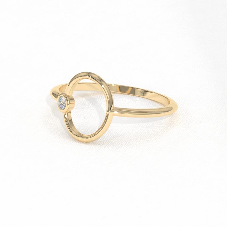 Puede incluir: Un anillo de oro con un dise&ntilde;o ovalado y un peque&ntilde;o diamante redondo. El anillo tiene una banda delicada y un acabado pulido. El anillo es una joya.