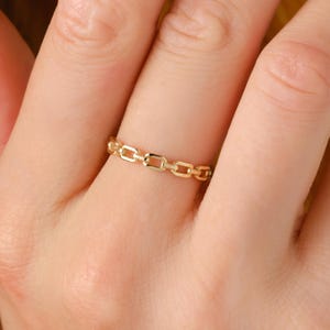 May include: A gold chain ring with a delicate design. The ring is worn on a finger.