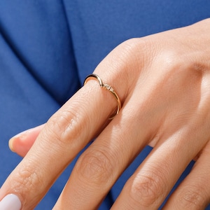 May include: A delicate gold ring with three small diamonds set in a curved band.