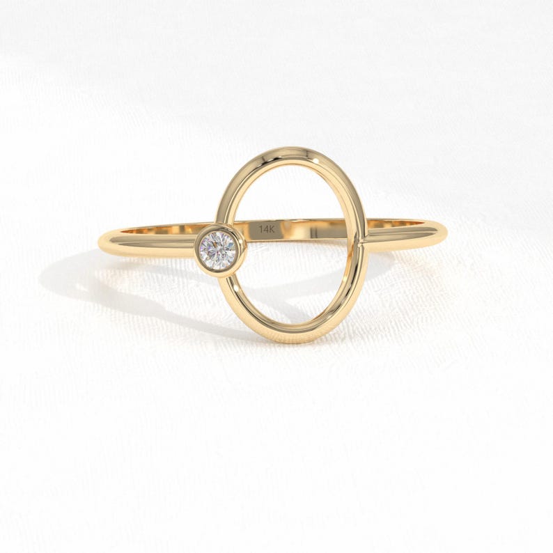 Puede incluir: Un anillo de oro con un dise&ntilde;o ovalado abierto &uacute;nico. Una peque&ntilde;a gema redonda y transparente est&aacute; engastada en un lado del &oacute;valo. El anillo est&aacute; marcado "14K".