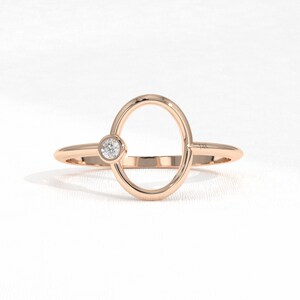 Puede incluir: Anillo de oro rosa con un dise&ntilde;o ovalado y una peque&ntilde;a gema redonda y transparente. El anillo tiene una banda delgada y un acabado pulido, con un dise&ntilde;o minimalista. El anillo probablemente est&aacute; hecho de oro de 14 quilates.