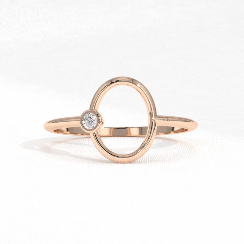 Puede incluir: Anillo de oro rosa con un dise&ntilde;o ovalado y una peque&ntilde;a gema redonda y transparente. El anillo tiene una banda delgada y un acabado pulido, con un dise&ntilde;o minimalista. El anillo probablemente est&aacute; hecho de oro de 14 quilates.