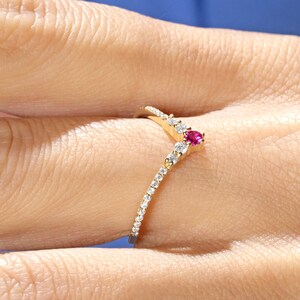 May include: A gold ring with a V-shaped band of small diamonds and a single pink gemstone at the point of the V.