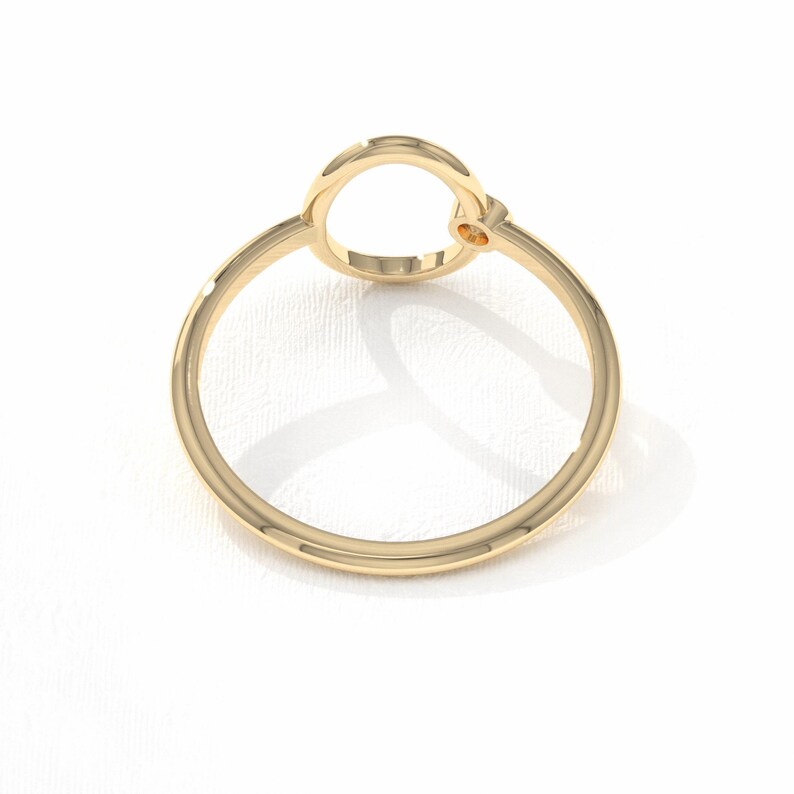 Puede incluir: Un anillo de oro con un dise&ntilde;o circular. El anillo presenta un gran c&iacute;rculo abierto conectado a la banda, con una peque&ntilde;a piedra de acento. El anillo est&aacute; sobre un fondo blanco, resaltando su acabado pulido.