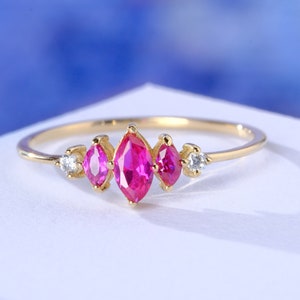 May include: A gold ring with three pink marquise-shaped gemstones and two smaller round white gemstones.
